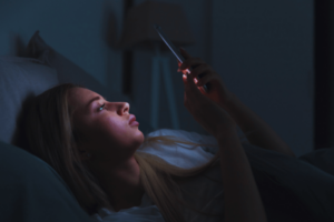 Exhausted woman lying in bed using mobile phone