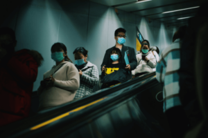 People on the escalator wearing masks and holding their smartphones during pandemic
