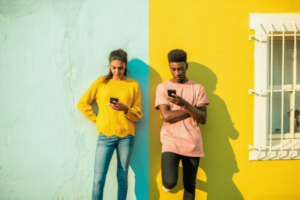 Two young people leaning on a wall using their smartphones