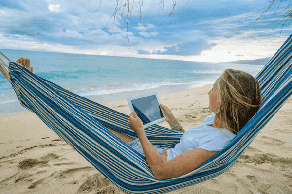 Digital nomad- Woman relaxing on hammock at sunset by the beach with digital tablet