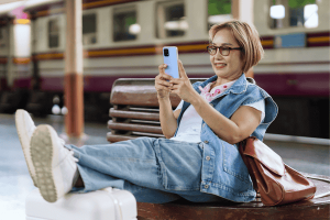 Asian older woman traveler using mobile phone train station plat
