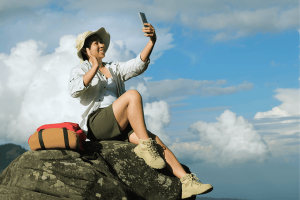 Happy traveling woman sitting on a cliff and using a mobile phone