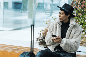 Hispanic Man Wearing Fedora Hat and Fur Coat Holding Smartphone