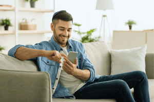Smiling jew man using smart phone sitting on couch
