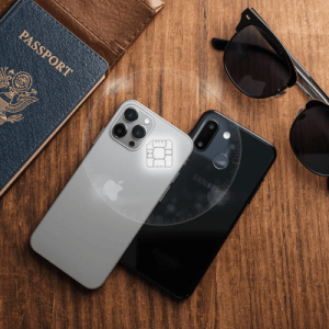Close-up of eSIM compatible phones including an iPhone and Samsung Galaxy on a desk next to travel essentials like a passport