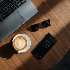Top-down view of a cafe table in Penang with a laptop, coffee, and a phone displaying a remaining data balance notification for an esim malaysia plan.