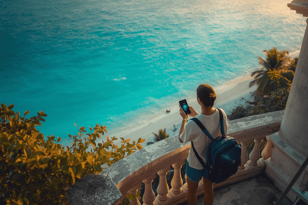 Traveler holding a smartphone with digital connection on a balcony overlooking a tropical Tulum beach in Mexico at sunset
