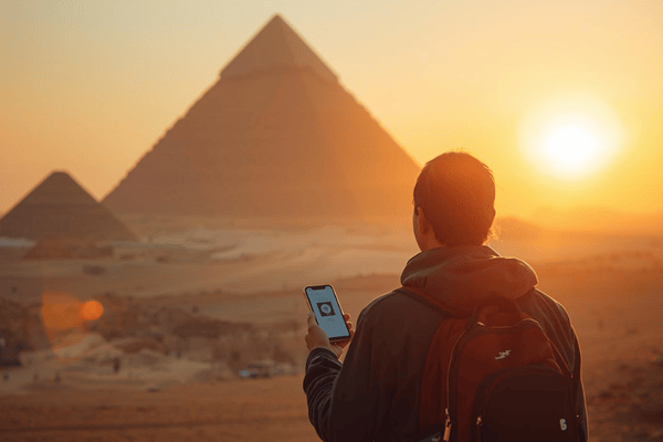 A traveler using a smartphone with the Great Pyramids of Giza in the background during a golden hour sunset