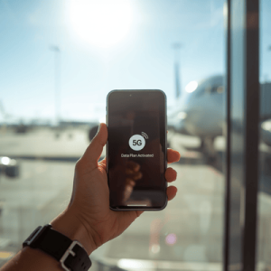 Traveler holding a smartphone with an activated eSIM data plan at an airport terminal overlooking an airplane
