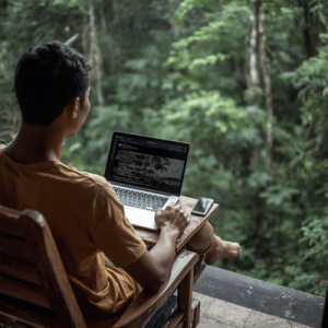 A remote worker using a laptop and phone hotspot on a balcony surrounded by tropical jungle greenery in Bali