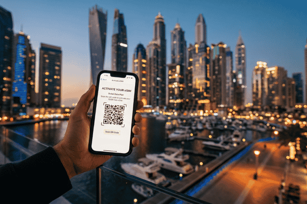 A person holding a smartphone displaying an eSIM activation QR code, with a blurred backdrop of the Dubai Marina skyline lit up at dusk